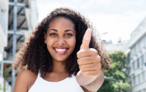 Young caribbean woman with curly hair in city showing thumb