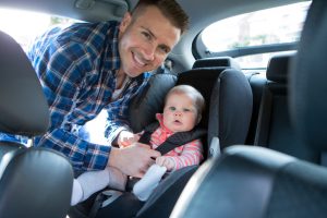 Father Putting Daughter In Safety Seat On Car Journey